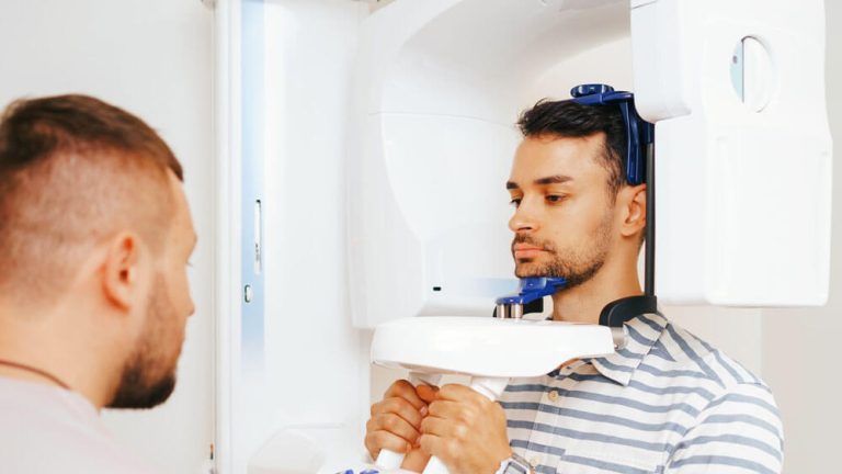 A male patient undergoing a CBCT dental scan, assisted by a technician in a clinical setting.